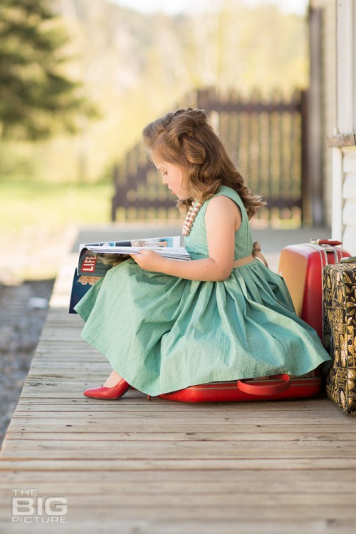 children's photography, birthday portraits, young girl in a green dress with rockabilly hair waiting at train station reading a magazine