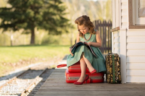 children's photography, kid's portraits, little girl sitting on suitcases at the train station reading a magazine with vintage hair