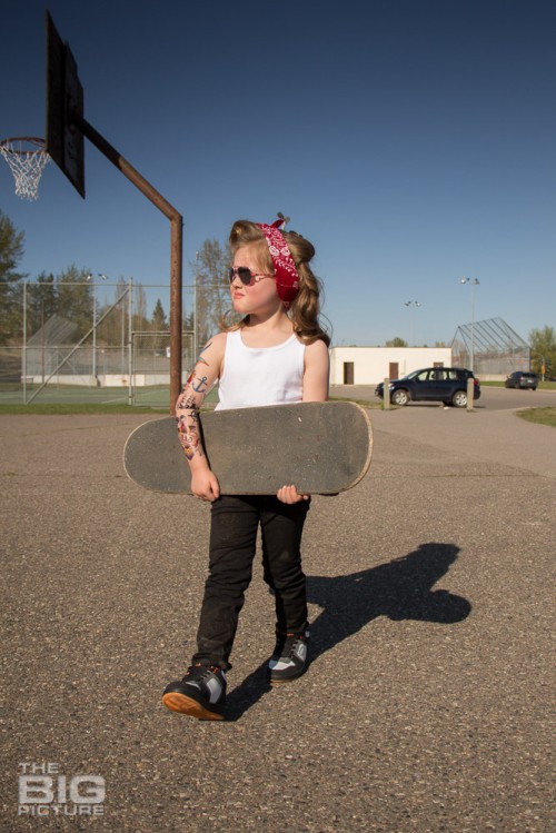 children's portraits, little skater girl with sunglasses and retro hair and fake tattoo sleeve carrying a skateboard in a skate park on a sunny day, children's photography, skater girl