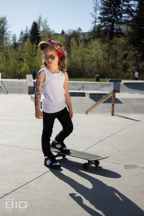 children's portraits, little skater girl with sunglasses on retro hair and fake tattoo sleeve standing on a skateboard in a skate park on a sunny day, children's photography, skater girl