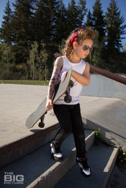 children's portraits, little skater girl with sunglasses and retro hair and fake tattoo sleeve holding a skateboard going down stairs in a skate park on a sunny day, children's photography, skater girl