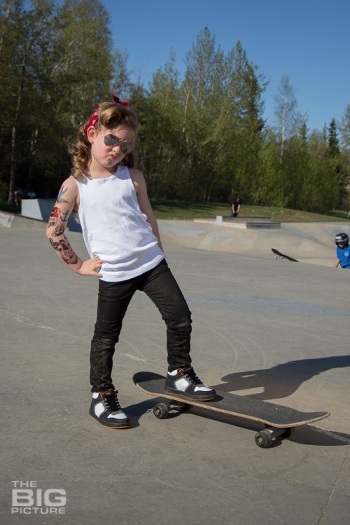 children's portraits, little skater girl making a duck face wearing sunglasses with retro hair and fake tattoo sleeve standing on a skateboard in a skate park on a sunny day, children's photography, skater girl