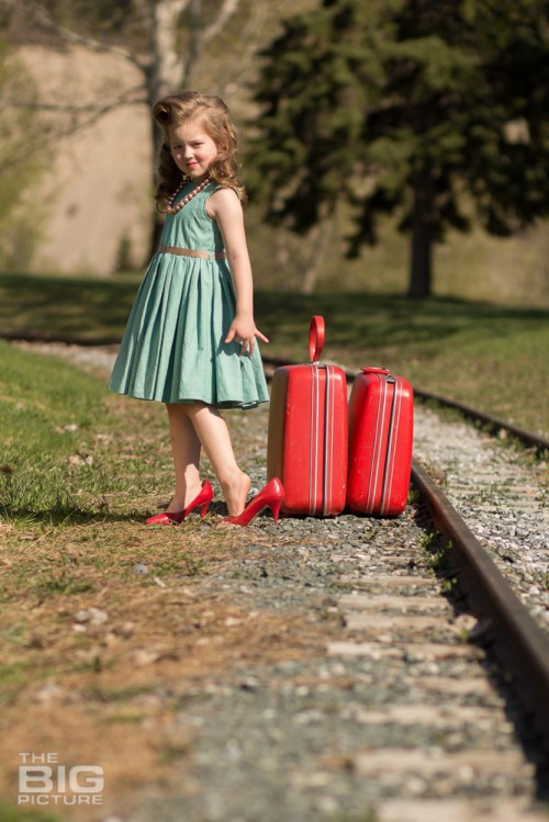 children's portraits, young girl with victory rollsl in red high heels with red luggage by railroad tracks